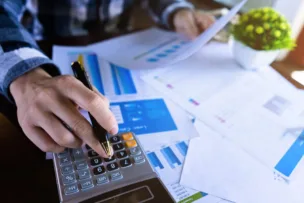 Person using a calculator and reviewing financial documents with charts and graphs on a desk, symbolising financial analysis or budgeting