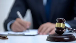 udge in a suit signing legal documents with a wooden gavel in the foreground on a desk.