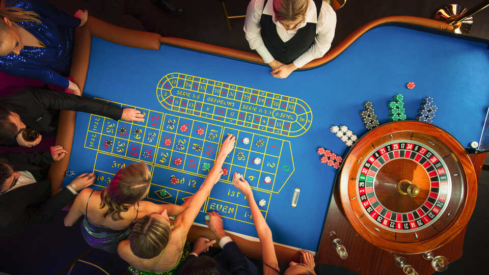 Overhead view of a lively casino roulette table with players placing bets and a dealer overseeing the game