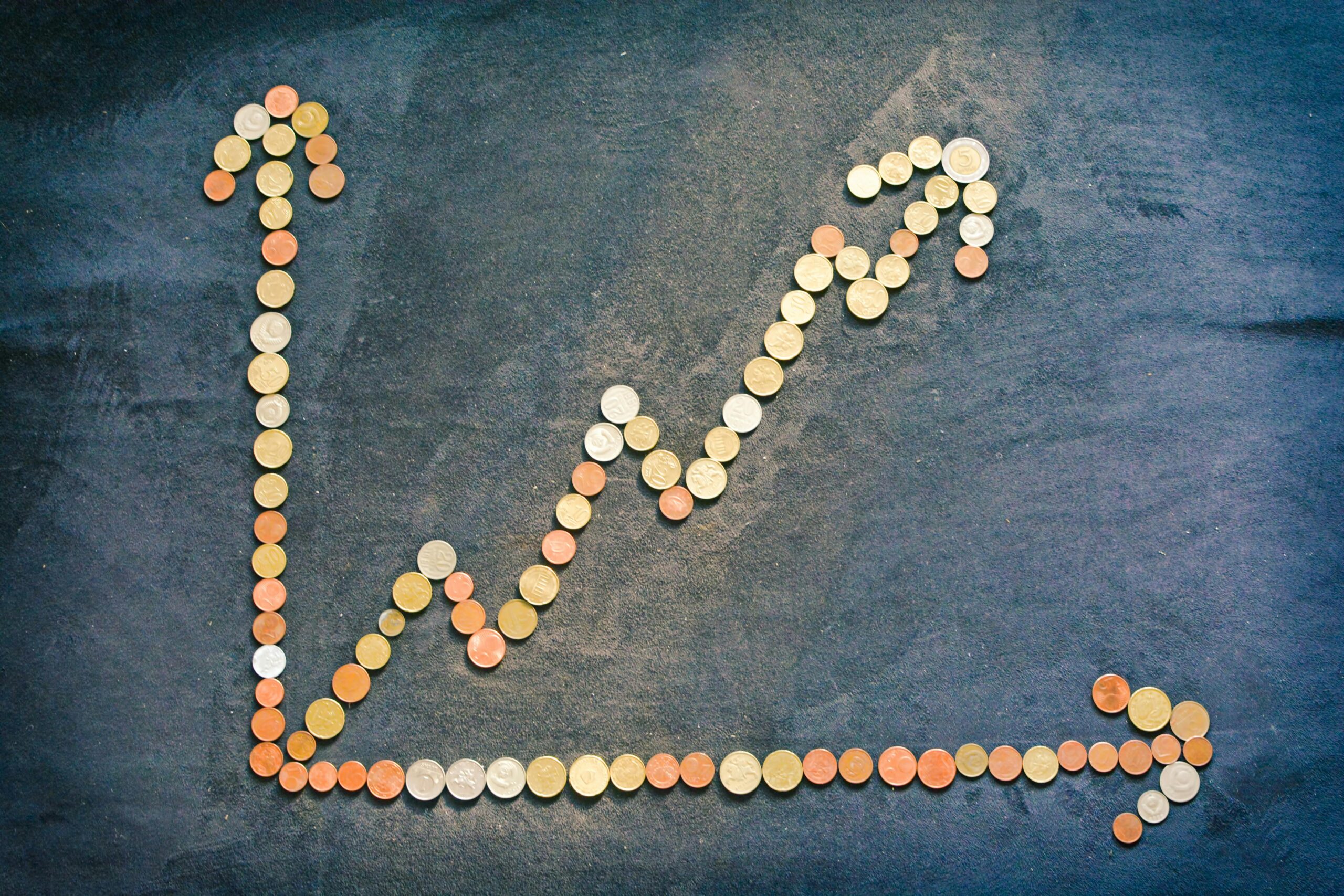 Upward trending graph made from assorted coins on a dark textured background, symbolising financial growth and investment.