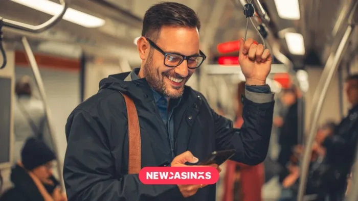 How UK Players Use Casino Apps During Commutes A man with glasses and backpack standing on a train or underground. He is holding a phone and looking at it whilst smiling, the New Casinos logo in the foreground.